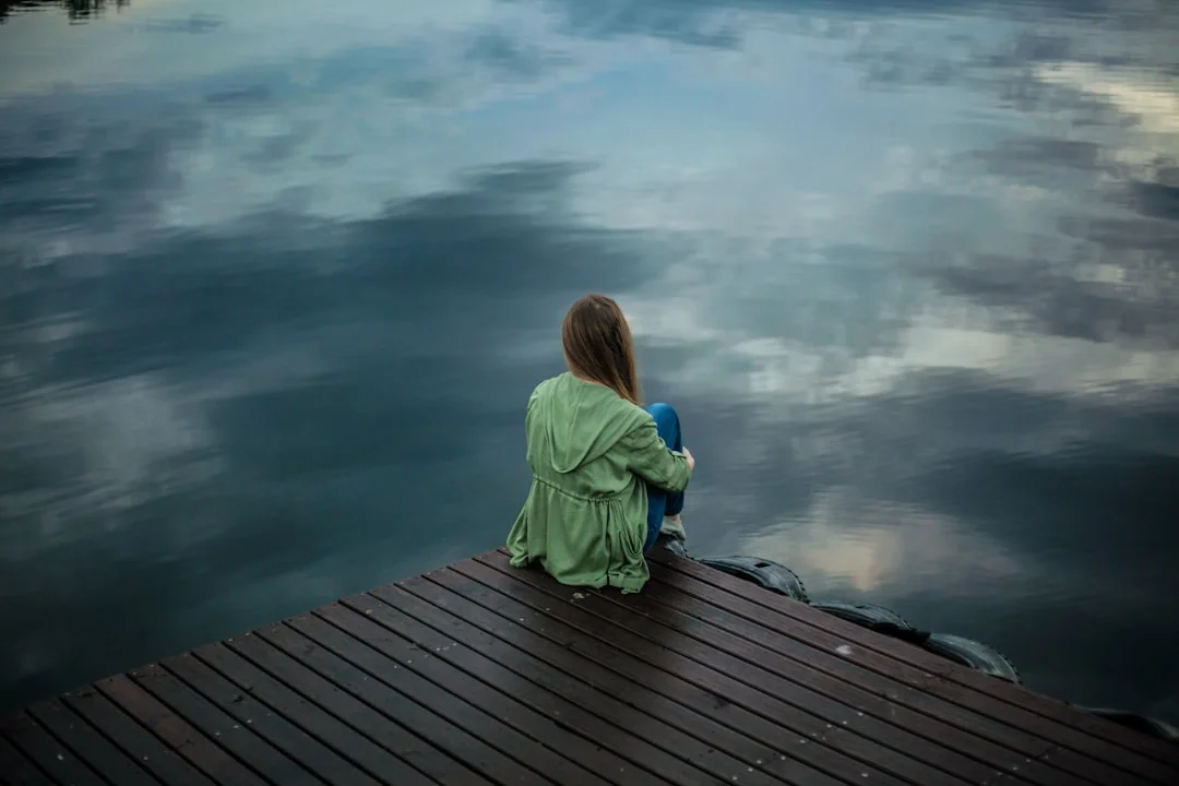 woman sitting on dock near body of water (Fot. Keenan Constance / Unsplash)