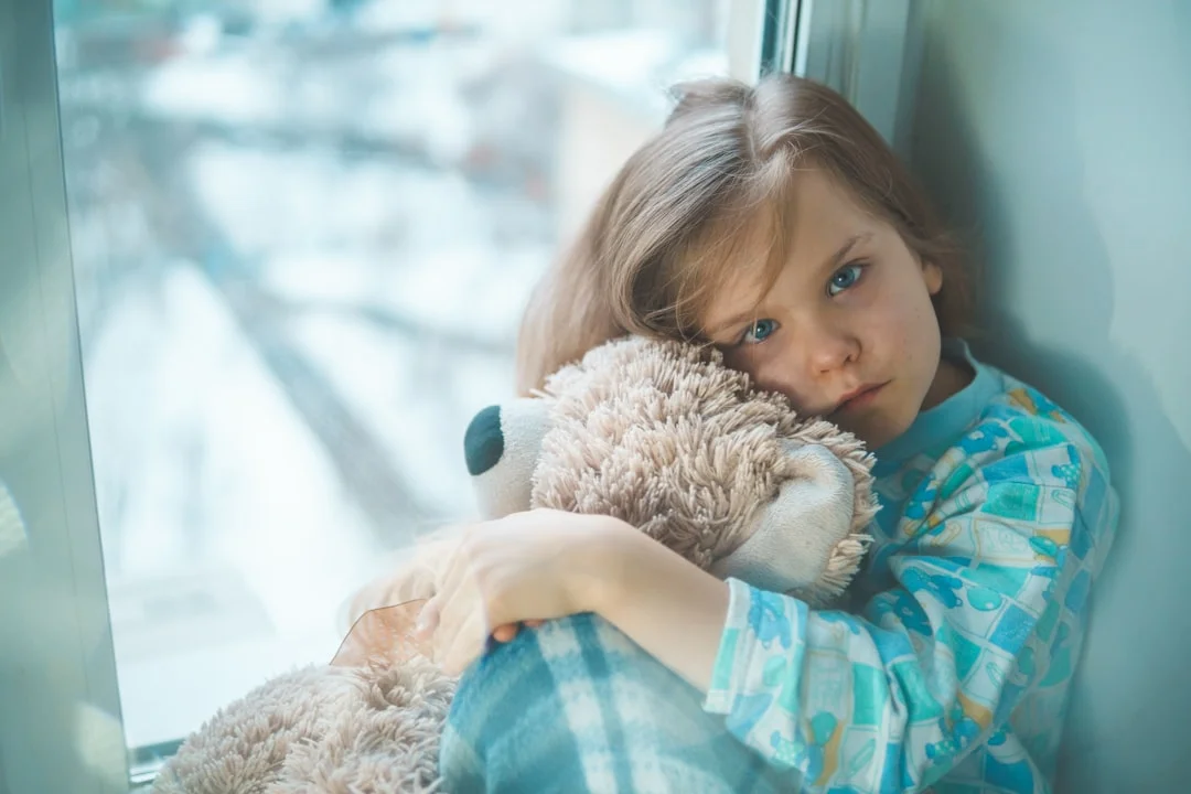 girl in blue white and red plaid shirt hugging brown teddy bear (Fot. Vitolda Klein / Unsplash)