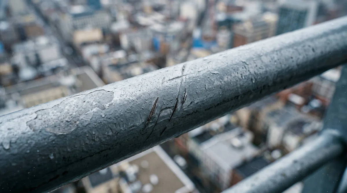 Zbliżenie na metalową poręcz balkonu z rozmazanym miastem w tle, akrofobia